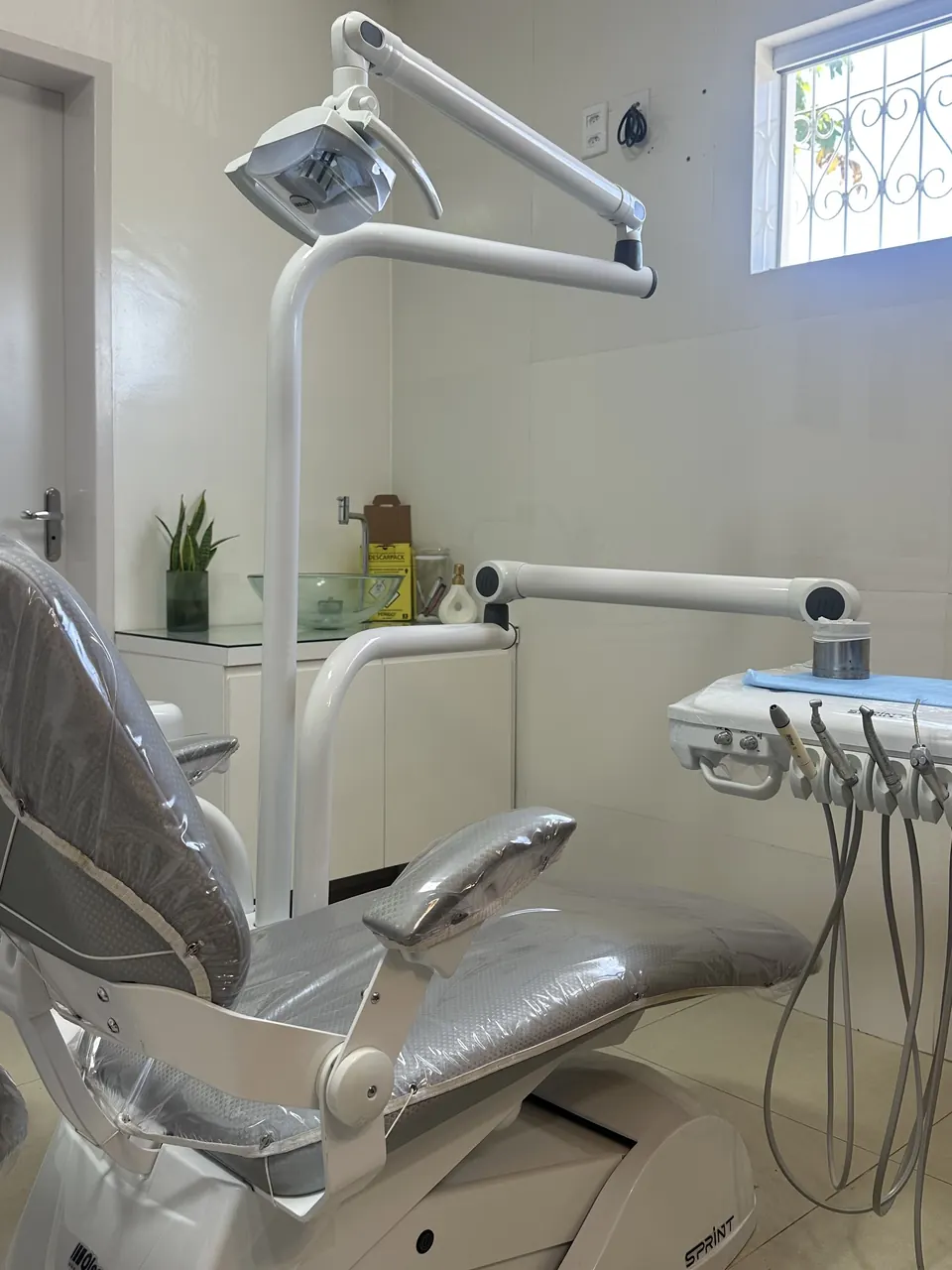Sala de atendimento com cadeira odontológica, refletor e janela